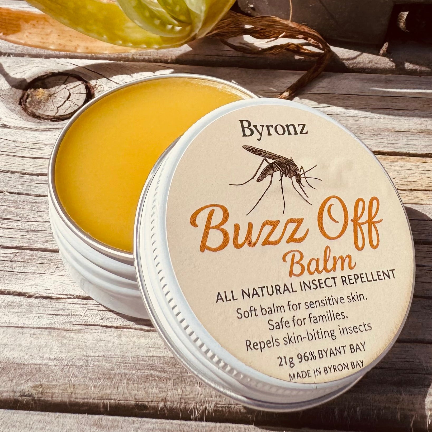 Byron's Buzz Off Balm container on a wooden surface with a plant in the background
